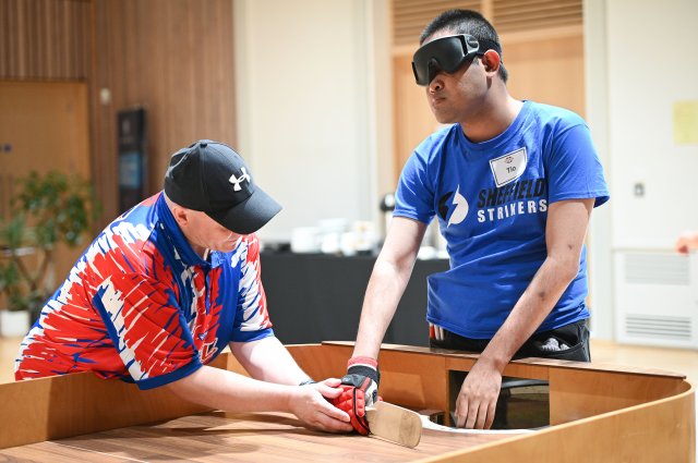 A male UK Showdown coach supporting a male player with his technique on the showdown table.