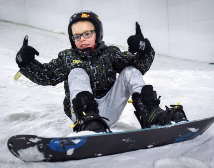 A young boy snowboarding on the slopes of the snowdome.